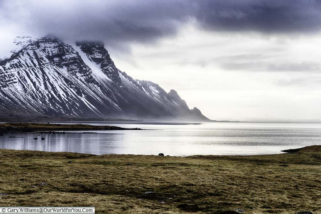 A snow-dusted mountain black mountain capped by brooding clouds on a misty morning just outside Höfn, in the southeast of Iceland.