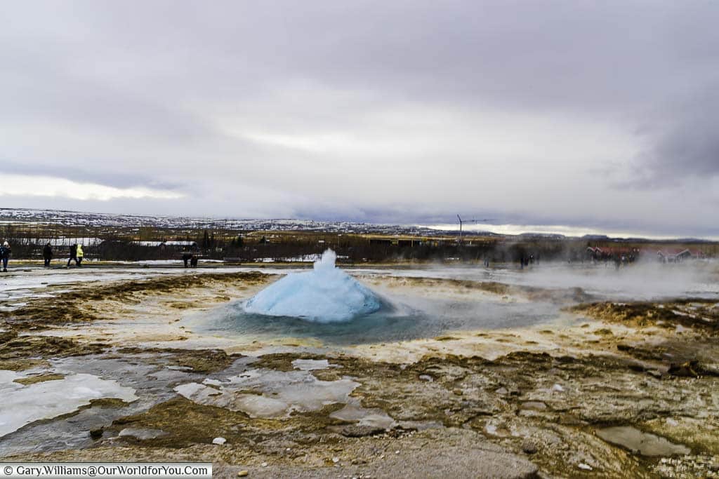 Water boiling up at the centre of the Strokkur geyser forms a blue bubble over the narrow hole in the earth's surface.