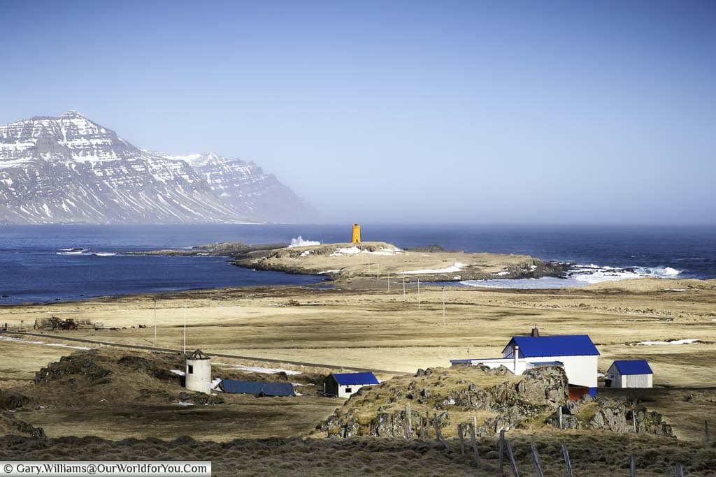 An orange lighthouse at the entrance to a ford in Eastern Iceland