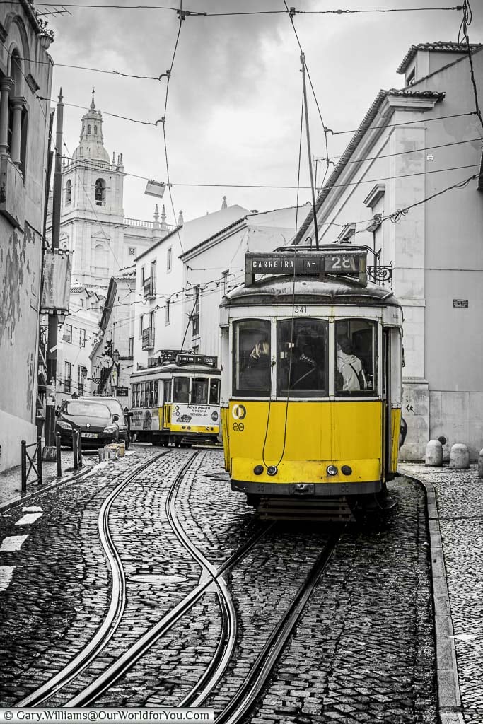 A desaturated black and white image of Tram 28 with just the yellow of the shot remaining as it makes its way through the narrow streets of portugals' captial, lisbon