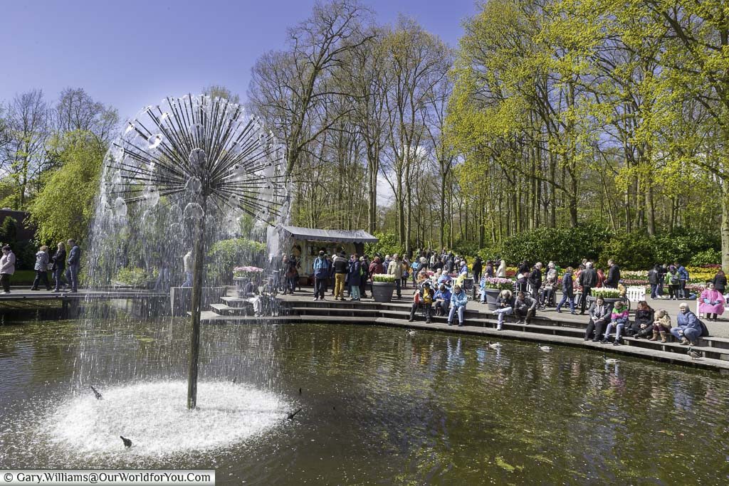An allium-styled water feature in the centre of a pond surrounded by seating at the eating area of keukenhof gardens in holland