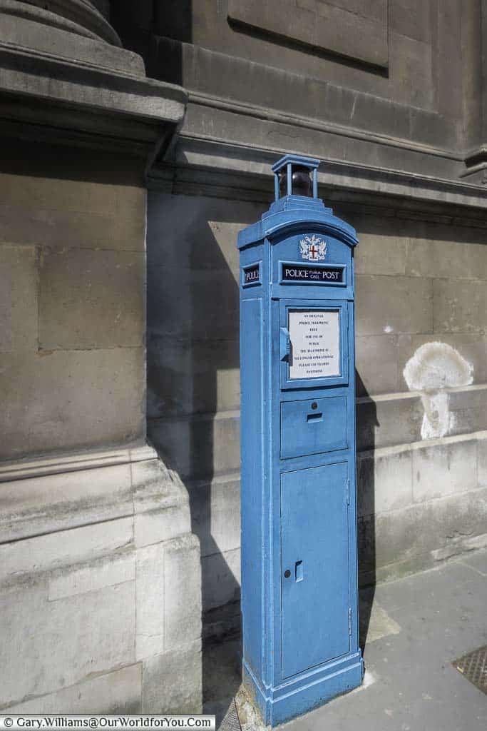 A brightly painted mid-blue Police post public call box next to a stone building