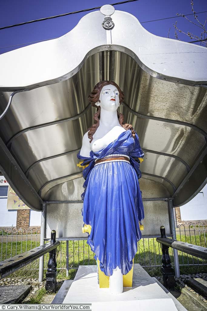 A brightly painted figurehead from HMS Arethusa of a red-headed woman, wearing a blue dress with a breast exposed