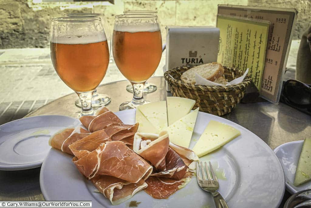 A plate of ham and cheese with a couple of beers at a table outside a restaurant in Valencia, Spain