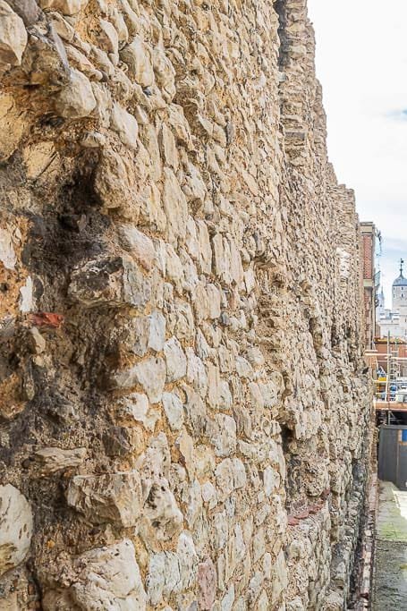 A close-up view of an exposed section of London's Roman wall, with the Tower of London just visible in the background.