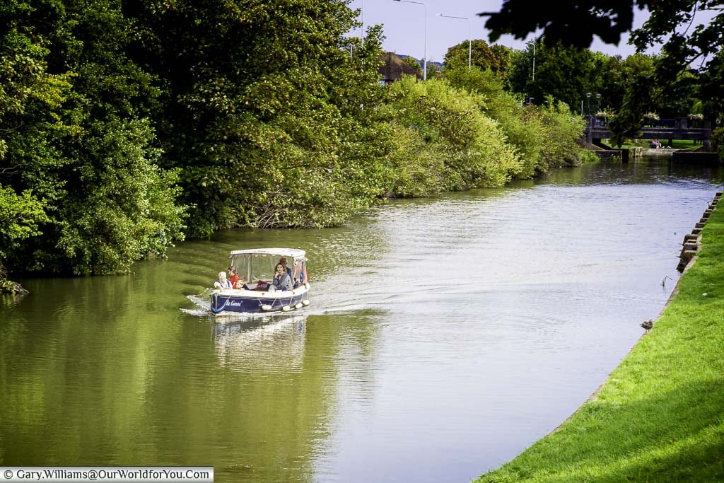 A small covered motorboat heading along the Royal Military Canal in Hythe, Kent