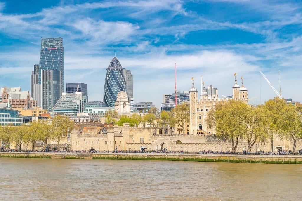 A view of the Tower of London from Tower Bridge with the River Thames in the foreground, and nestled next to the Tower of London are the skyscrapers of the City of London.