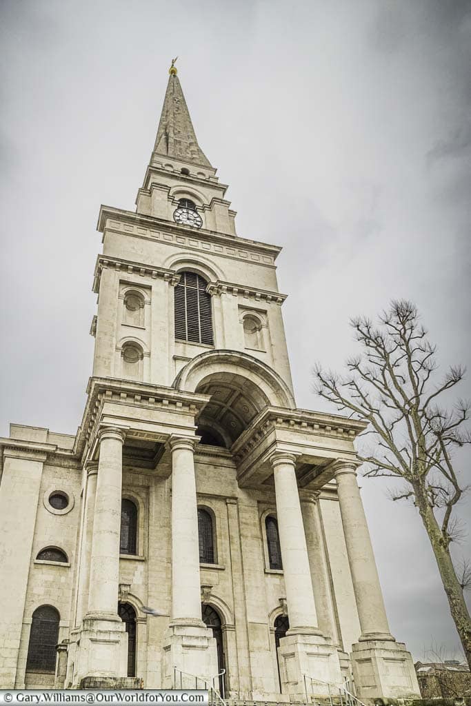 The impressive entrance and spire to Christ Church, Spitalfields. A tall cream stone church, with 4 huge columns at the entrance leading up to a pointed bell-tower.