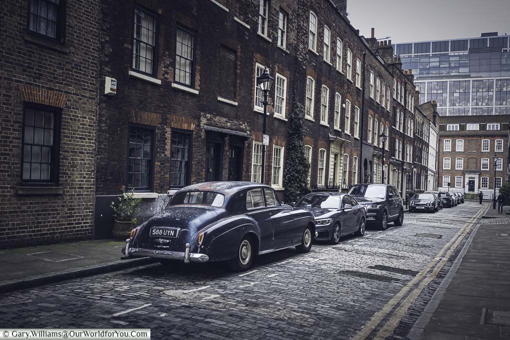 Elder Street, in the north of the Spitalfields district. A cobbled street of brick build Georgian terraced 3-storey houses. A classic 1950's Bentley is parked in a prime place.