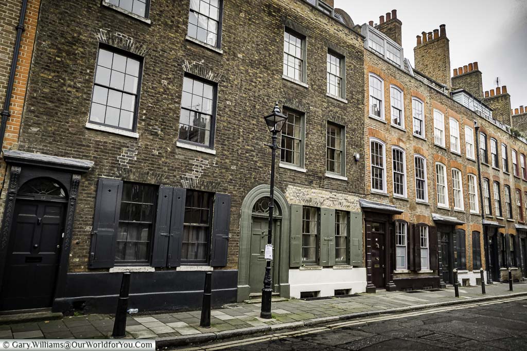 A view of the elegant Wilkes Street, Spitalfields, with its terraced 3 storey brick-built houses with shuttered windows, and cast iron bollards & lamp posts in a scene that hasn't changed since Dickensian times.