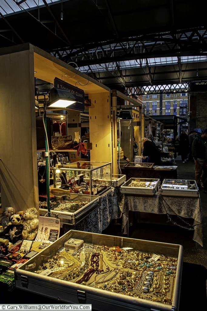 A stall selling all sorts of unique items, some in glass display cases, within the Spitalfields market.