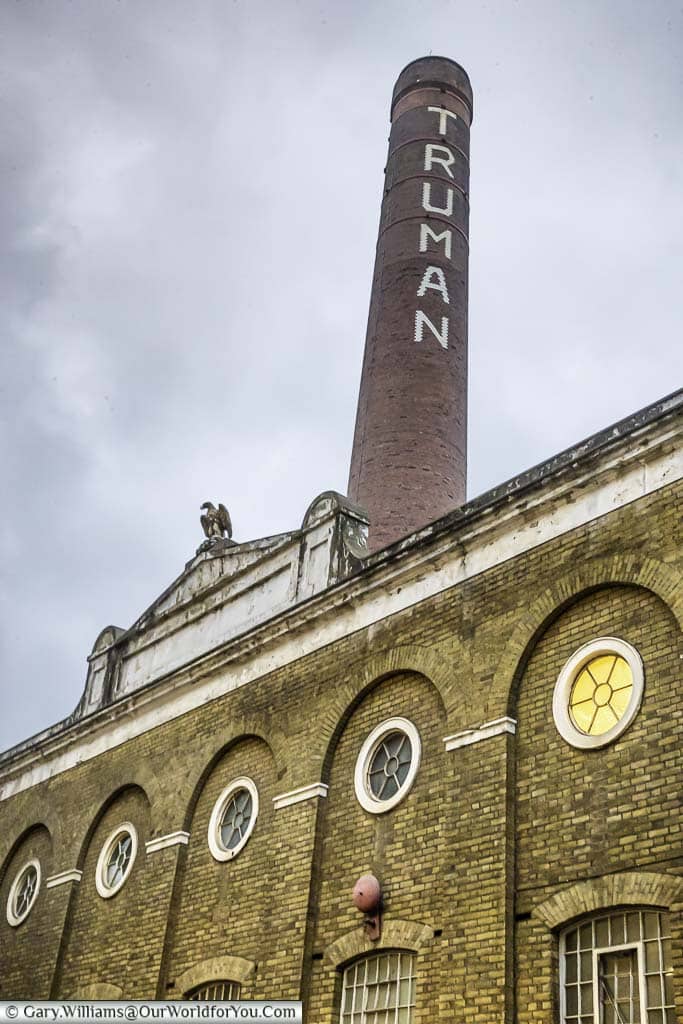 The brick building, and huge chimney stack, of the Truman's Brewery with its eagle statue. The Chimney has the name of the brewery painted in large white letters down the tower.