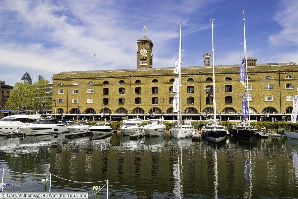 The Saint Katharine Docks in London, next to Tower Hill, with small, luxury, private boats moored in front of a historic warehouse building.