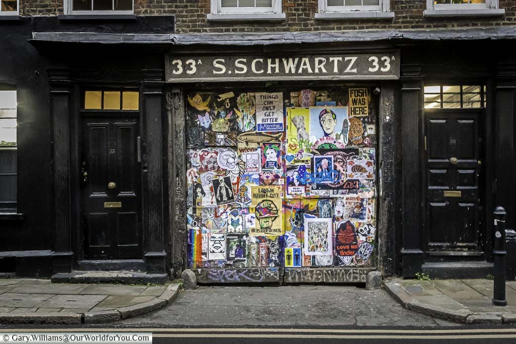 The entrance to 33a Fournier St in East London un the signage for S.Schwartz. The wide gateway used to be a diary but has now become a street art installation featuring posters of work commentating on social issues.