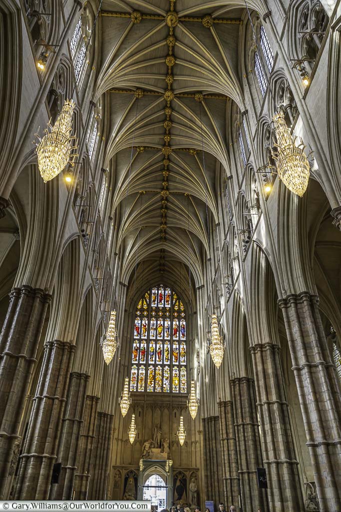 A view of the western end of Westminster Abbey Nave with ornate chandeliers hanging from the vaulted roof.