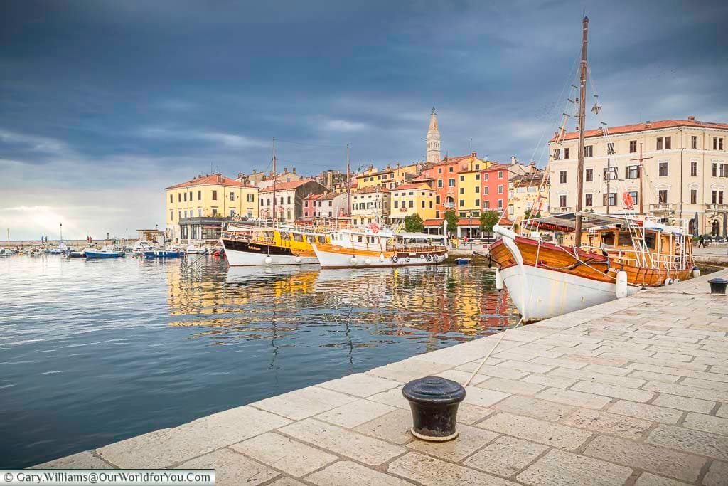 The quayside view at Rovinj, Croatia, under brooding skies with classic boats and colourful buildings in the background.