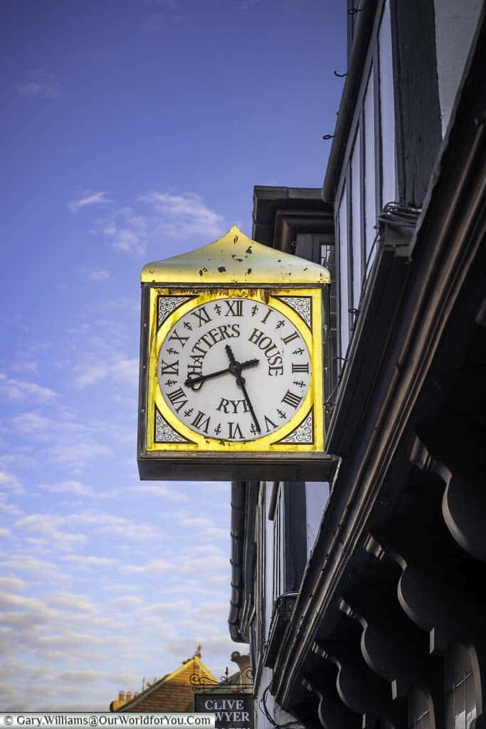 A slightly weathered gold gilded clock projecting from the former charter's house on rye high street in east sussex