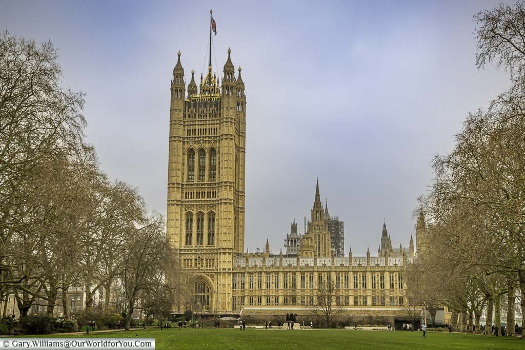 The Palace of Westminster, from Victoria Tower Gardens, with a Union Flag flying over the Victoria Tower.