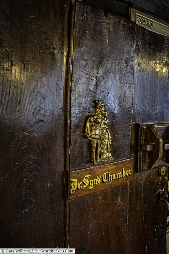A brass plaque depicting the fictitious character of Dr Syn, affixed to a heavy wood door at the entrance Dr Syn's Chamber at the mermaid inn in rye, east sussex