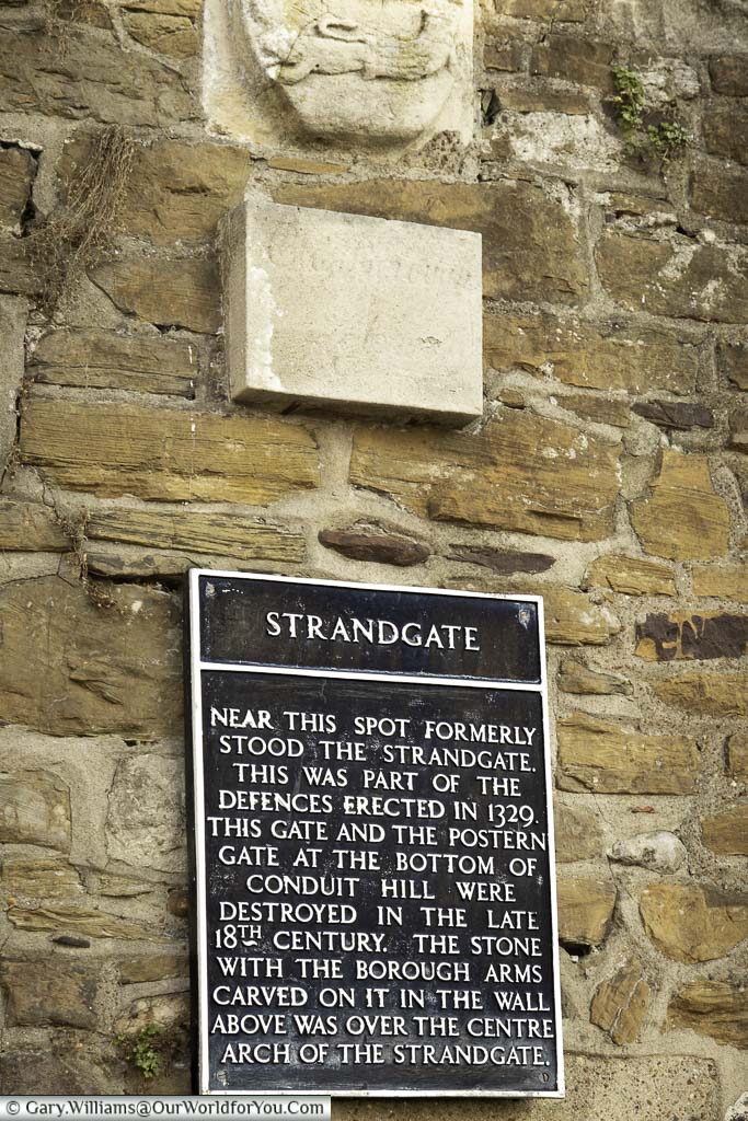 The iron plaque attached to a stone wall where the strandgate would have once stood in rye, east sussex detailing the town gate's history.