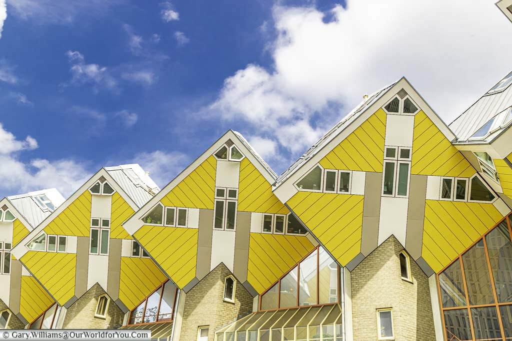 The iconic bright yellow cube houses are set against a blue sky with fluffy clouds in Rotterdam, Holland