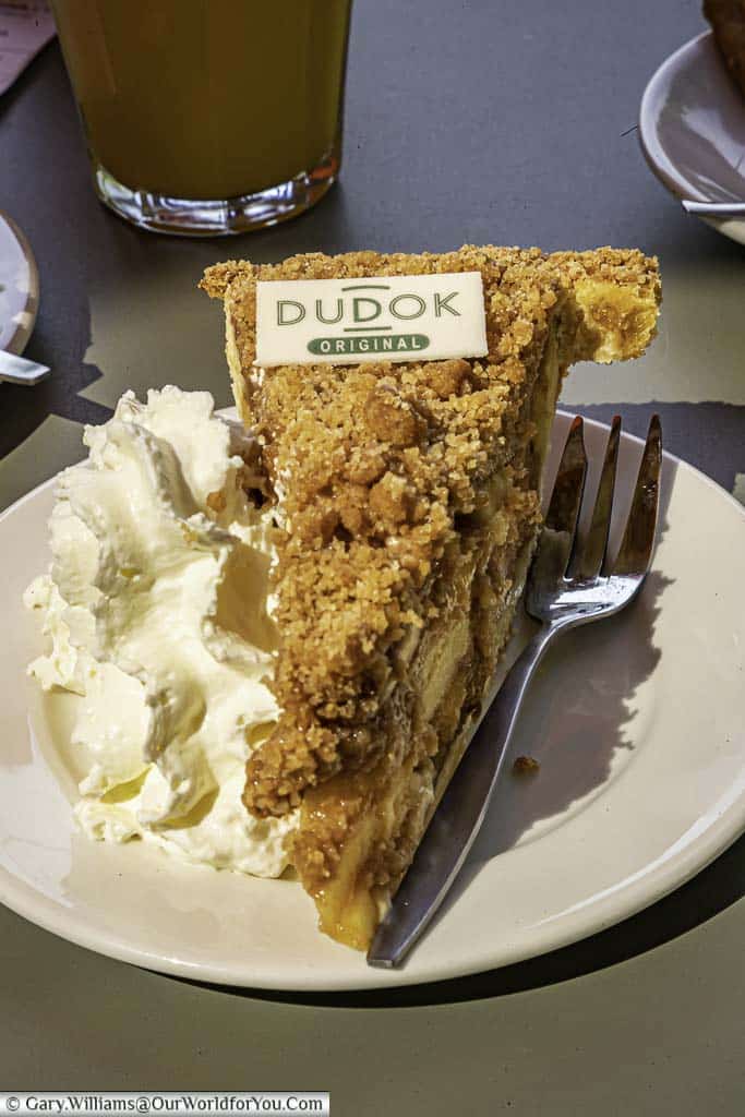 A slice of dudok's original apple pie, served with an ample helping of whipped cream on a china plate in rotterdam