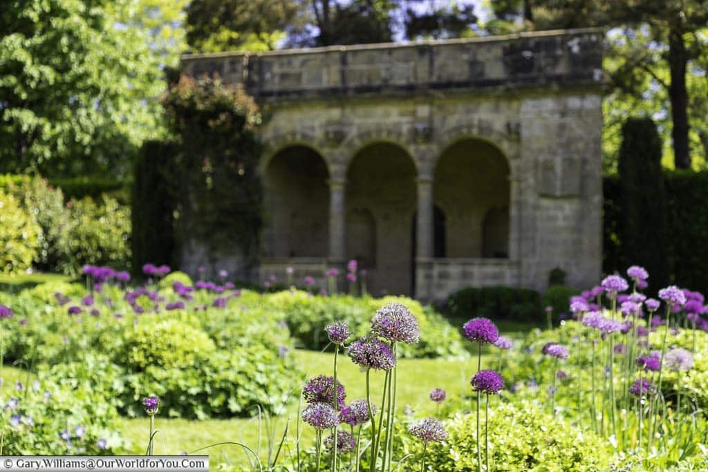 A smattering of purple alliums withing the circular sunken garden in front of a stone loggia at nymans house and gardens in west sussex