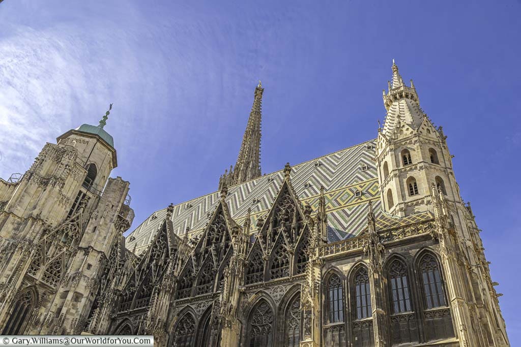 Looking up at St. Stephen’s Cathedral on a bright sunny day with clear blue skies. The detail in the gothic architectures is impressive with its coloured tiled roof.