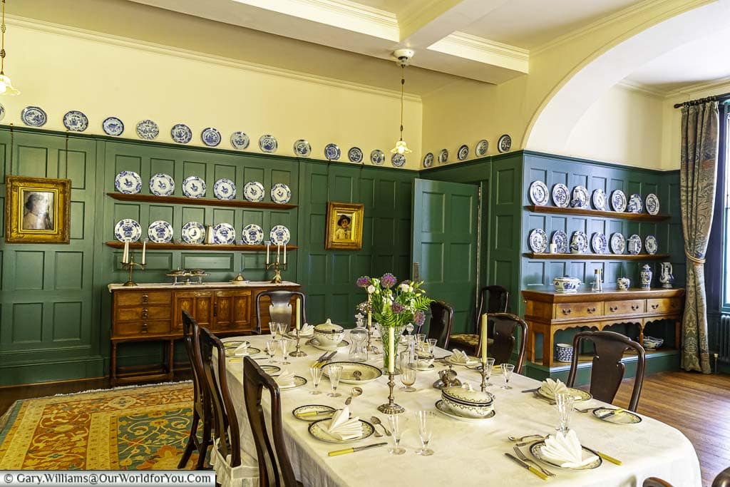 A table set for six in the centre of an arts and craft styled dining room with ivy green wood panelling at standen house in west sussex