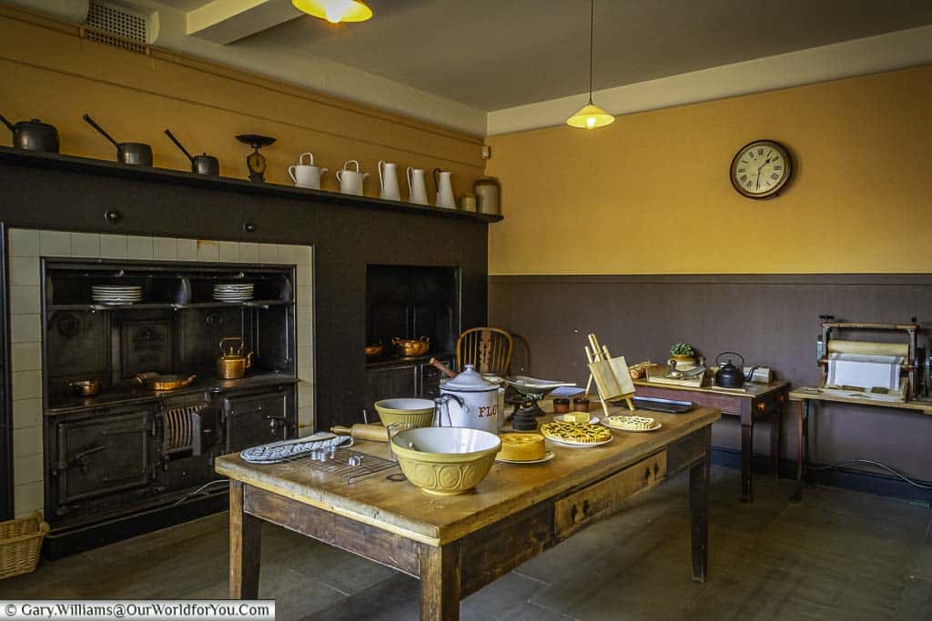 The spacious kitchen with a large table in its centre in front of a gunmetal grey range with copper pots set on top at the national trust's standen house in west sussex