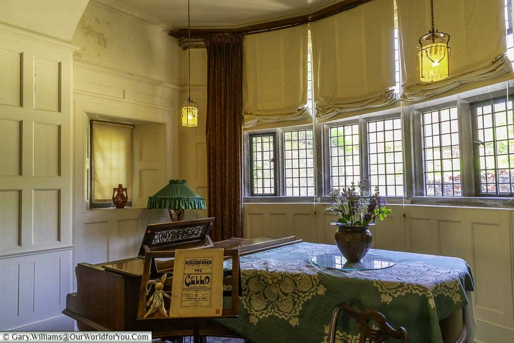 the living hall with a grand piano, a table, and a vase of flowers in standen house, west sussex