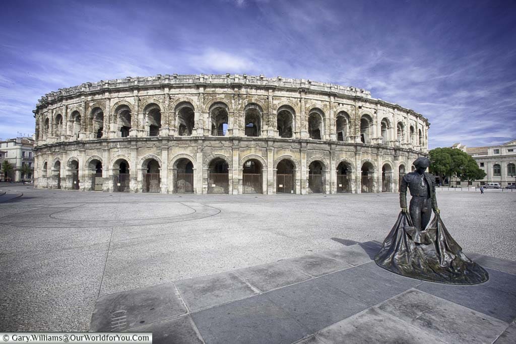 The brass statue of a bullfighter in front of the complete, two-storey, Roman arena in Nîmes.