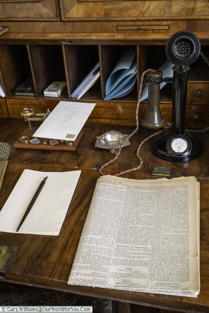 An early 20th century phone in front of a newspaper, pad and pen, on a wood wooden bureau in the telephone room of lamb house in rye, east sussex