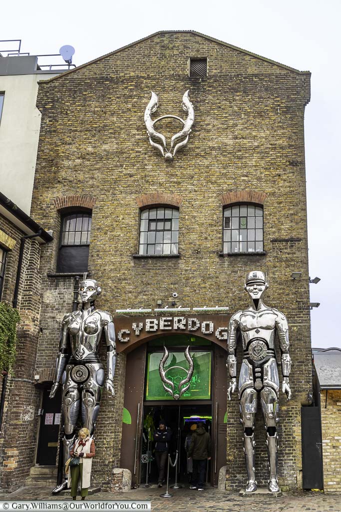 Two 6 metre tall metallic android figures flanking the entrance to Cyberdog fashion store, in one of the old industrial buildings in Camden Market.