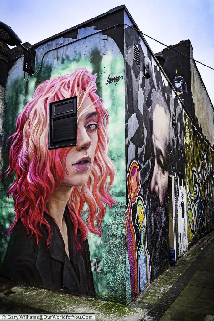 A near photo quality mural of a young woman with red & purple hair on the end of a building in Hawley Mews, Camden.