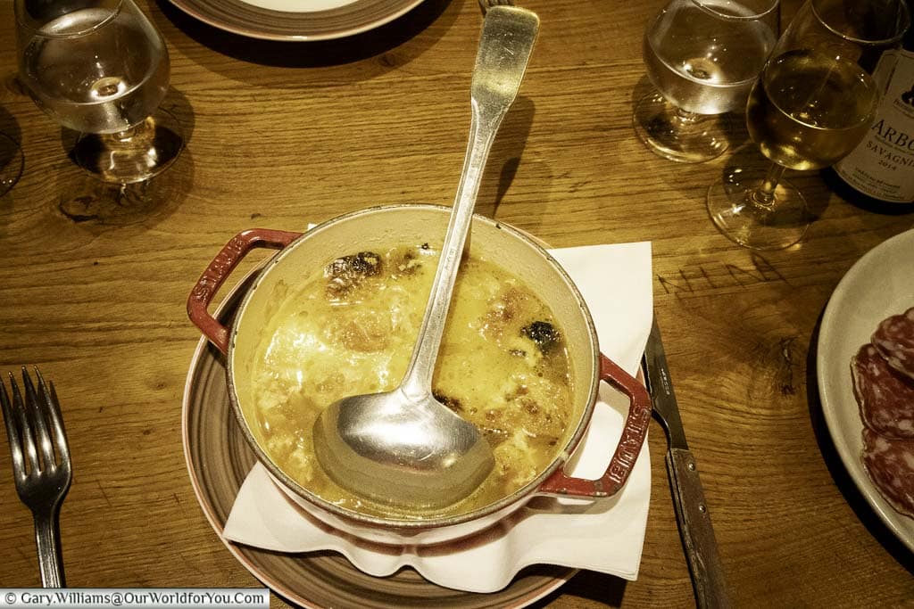 A large bowl of French Onion soup served in a cast iron cooking pot with a ladle to help yourself.