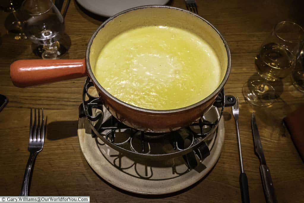 A bubbling pot of cheese fondue served in a cast-iron saucepan over a low heat.