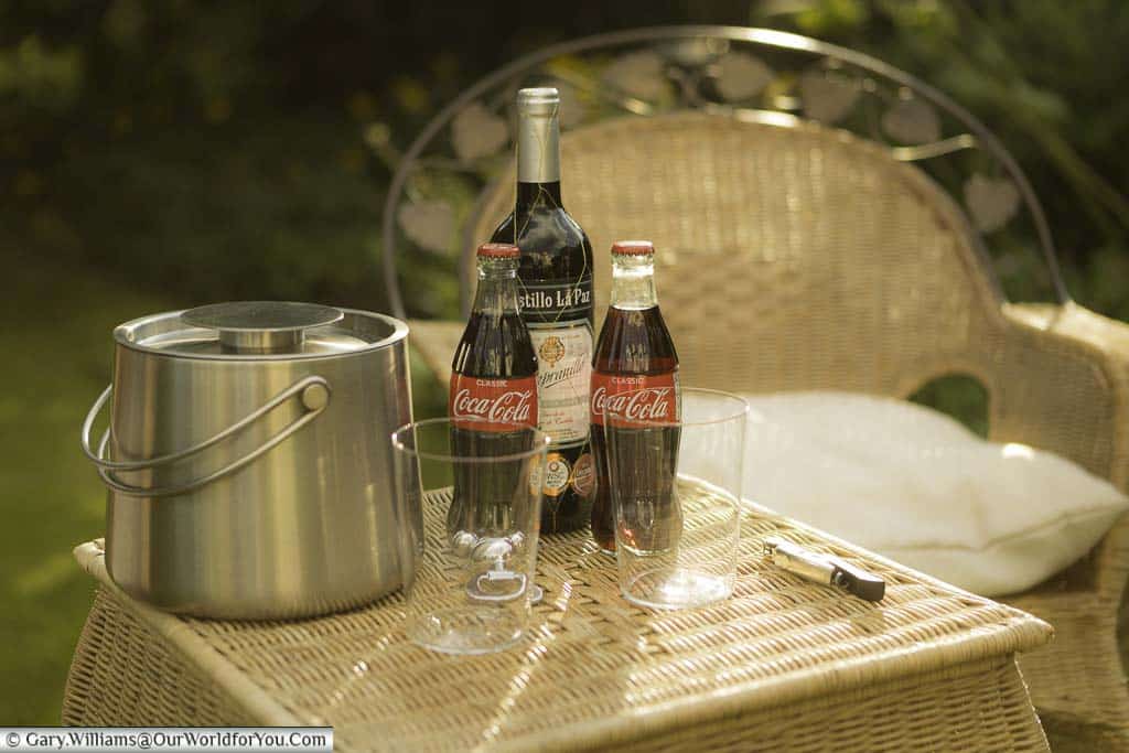 Two large straight glasses , two bottles of coke, a bottle of spanish red wine and a bucket of ice, the basic ingredients for a kalimotxo or calimocho, on a table in our garden