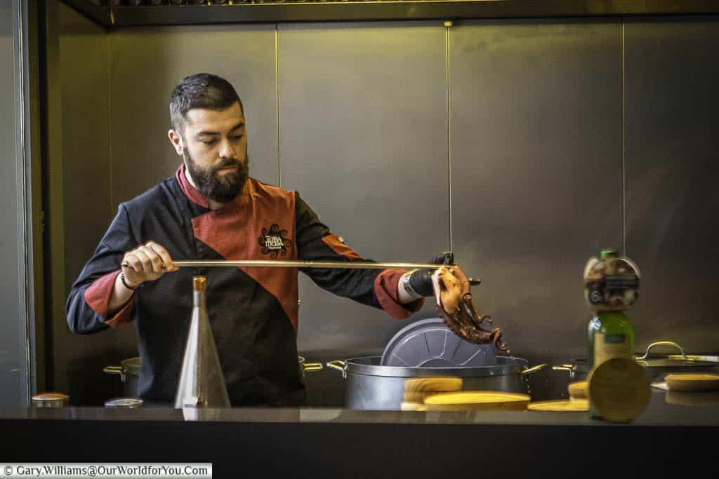A Spanish chef, pulling a skewered octopus from a pot of boiling water