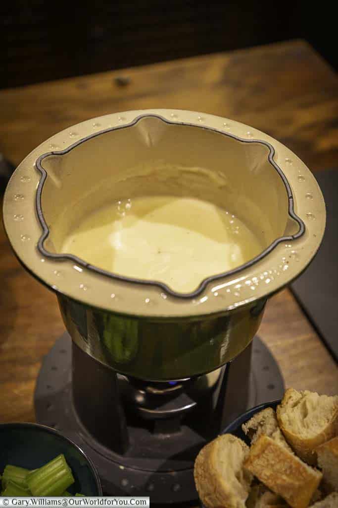 Our cast iron fondue pot, half-filled with a bubbling cheese fondue, with a pots of chopped celery & cubed french bread