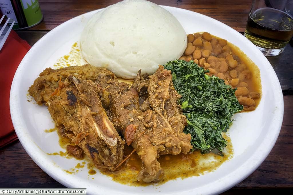 A plate of a rustic beef stew, with green leaves, beans & the Zimbabwean staple, sudza.