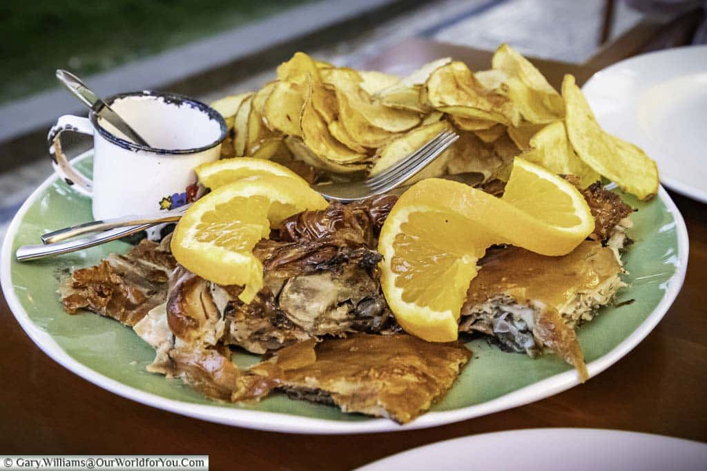 A plate of suckling pig, with its crispy skin, served with potato crisps and a twist of orange, in Porto