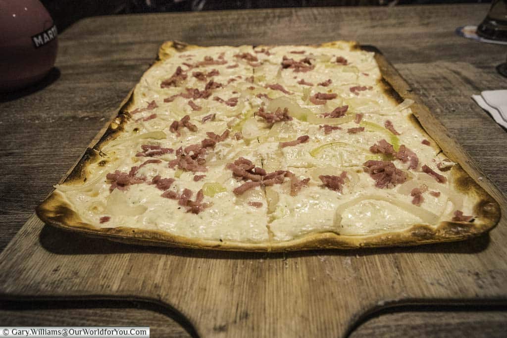 The traditional Alsatian dish of Tarte flambée, served on a wooden serving slice to be shared.