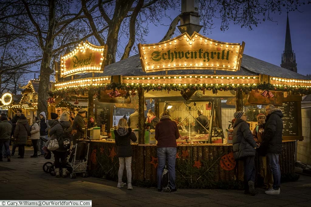 A grill stall on the quayside Christmas market at dusk, selling a variety of grilled sausages.