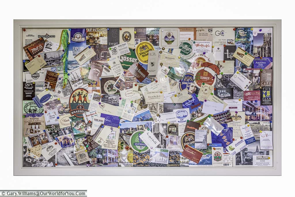A board in our kitchen containing business cards, beer mats, postcards, menus and other mementoes from our travels