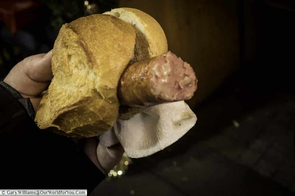 Gary holding a bread roll containing a German cheese sausage. The cheese sausage is the normal pork variety blended with cheese, so it oozes from the sausage.