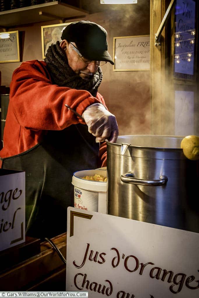 A mature man, wrapped heavily against the cold ladling out hot spiced orange juice at a stall in the Christmas markets.