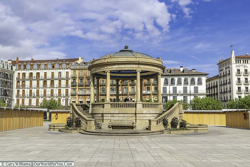 The sandstone-coloured bandstand in plaza del castillo, pamplona, surrounded by tall, historic buildings on all sides.