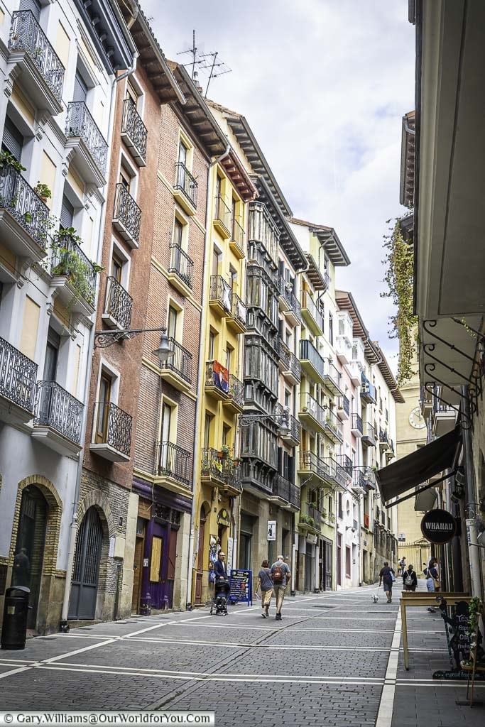 The narrow cobbled lane of calle curia, lined on either side by colourful, historic, balconied, 5-storey buildings in the centre of pamplona in spai