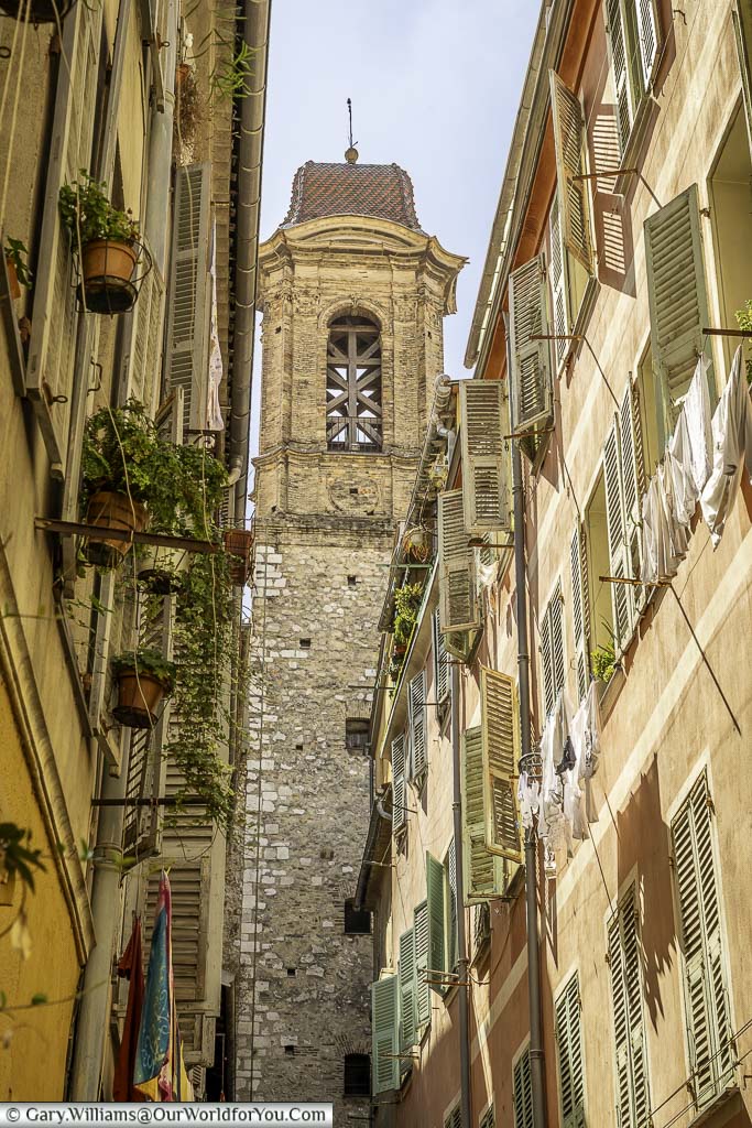 Washing hanging from the windows of traditional apartments in central nice with a church bell tower at the end of a narrow lane